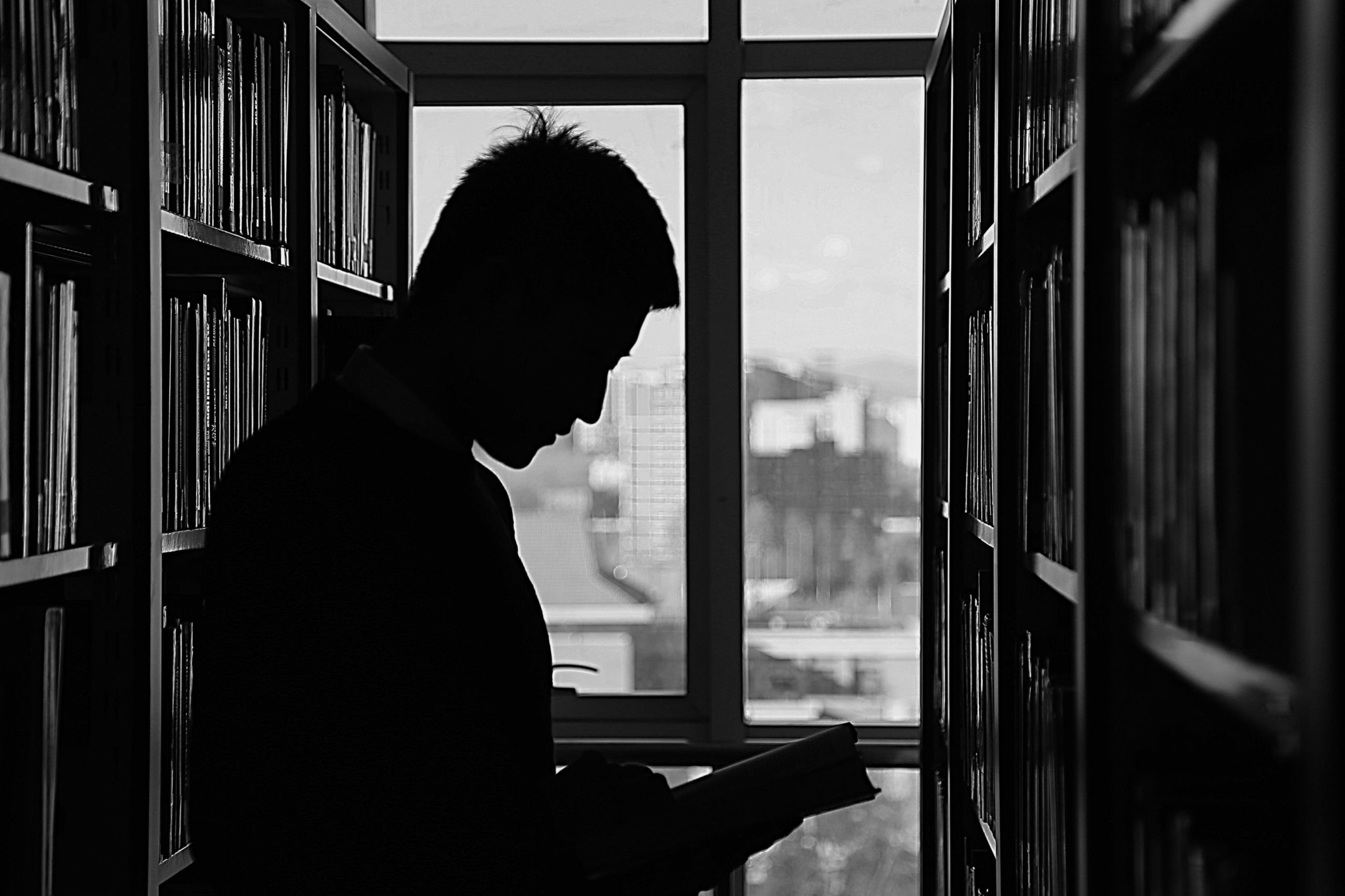 Silhouette of man in library reading book in aisle of books.